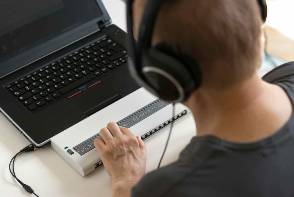 A man using a braille keyboard with a laptop.