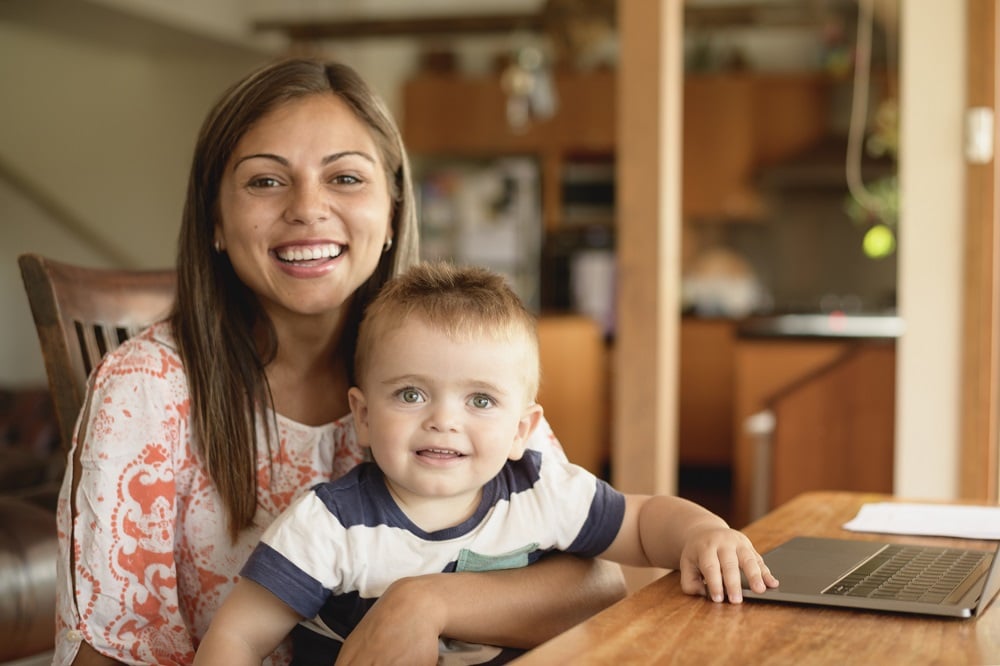 A mother and her toddler sitting at a table smiling.