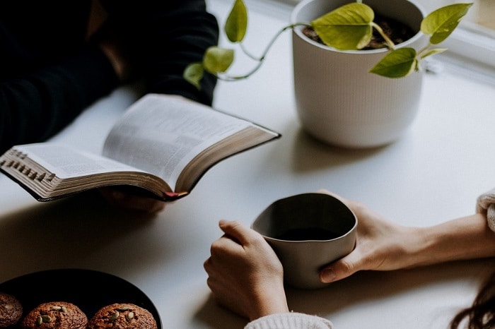 Two people sitting opposite each other - one is holding a book, one is holding a cup of coffee