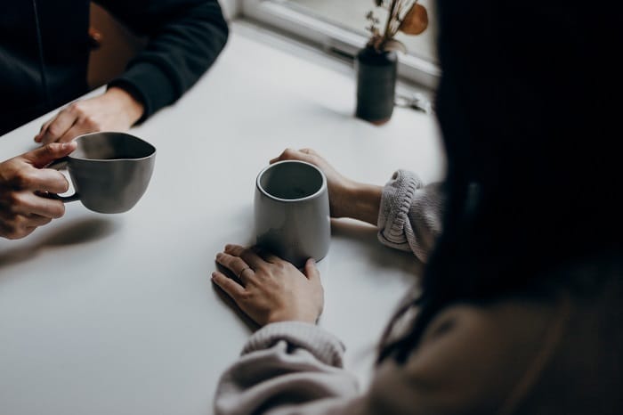 Two people sitting opposite each other at a table holding cups of coffee