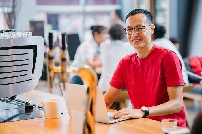 An image of a man in a red t-shirt at a laptop