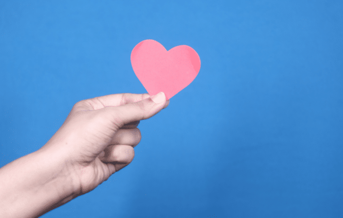 A hand holds up a red, heart-shaped paper cut out.
