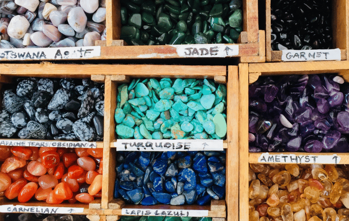 A wooden tray with compartments holds an array of colourful crystals including amethyst, lapis lazul and turquoise.