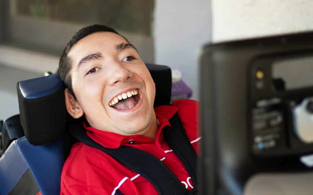 A smiling young man in a red t-shirt uses his eye gaze device.
