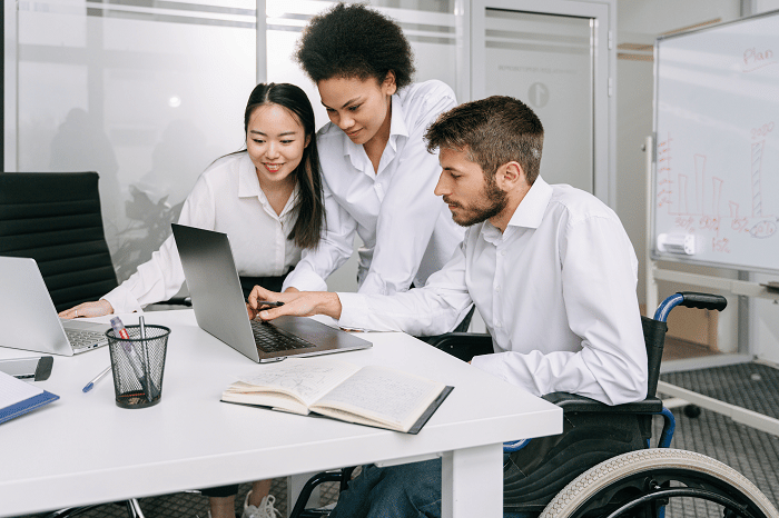 Three people in an office setting, working on a laptop.