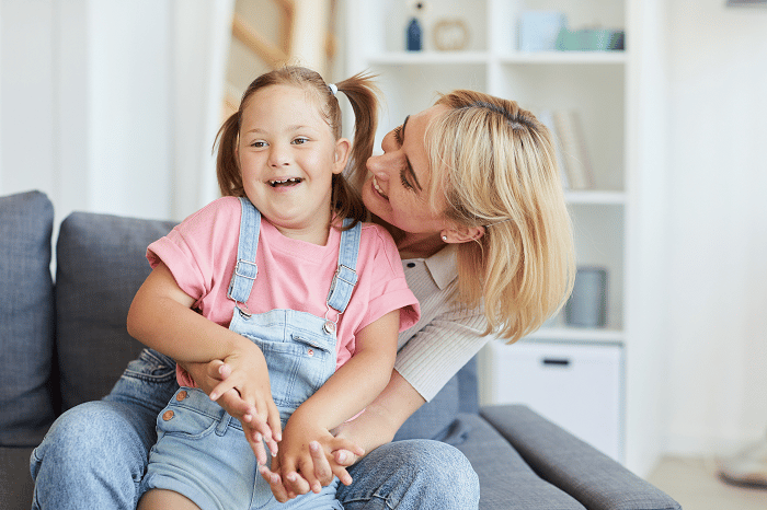 A woman and a young girl, sitting on a couch, laughing.