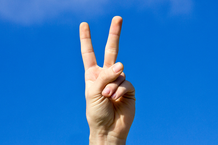 A hand signing the number two, with the sky as the background.