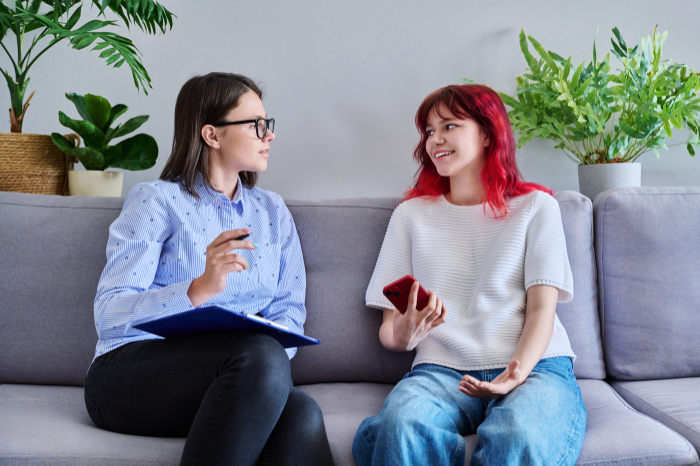 Two women sitting on a couch talking.