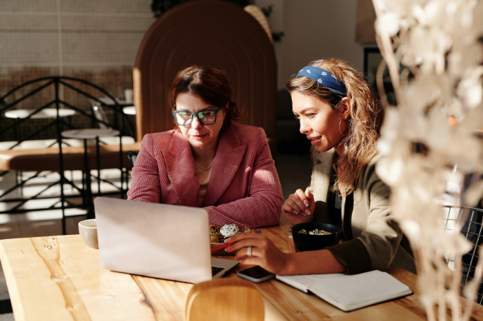 Two people in a cafe sit at a table whilst working together on a laptop.