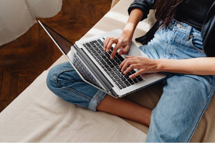 An open laptop rests on a person's lap as they type.