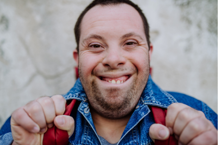 A man wearing a backpack smiles at the camera.