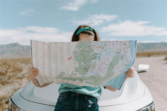 A person sitting on the bonnet of a car inspects a large map.