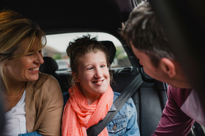 A smiling child with disability sits in a car with her parents.