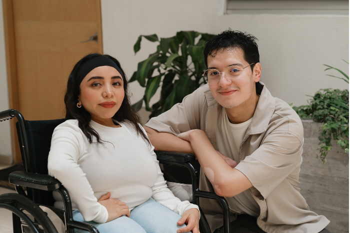 A person sits confidently in their wheelchair, with a friend by their side.