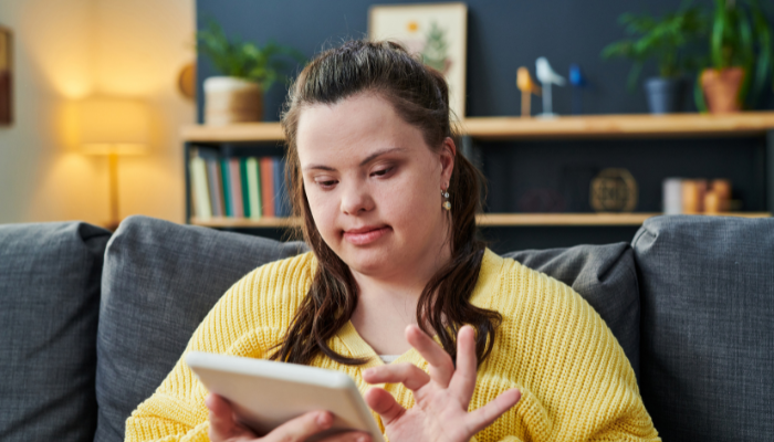 A close up of person in a yellow sweater on a grey couch using an iPad.