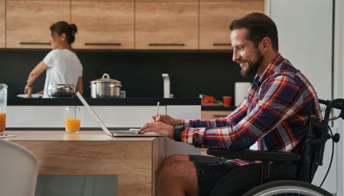 A side-view shot of man in a wheelchair sitting at a table using a laptop.