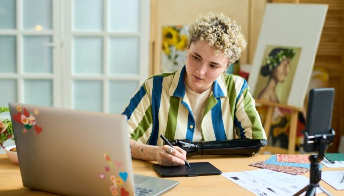 A person with disability sitting at a desk in front of a laptop using a digital writing pad.