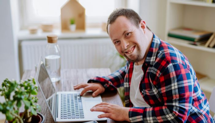 A man at a desk using a laptop looking to camera.