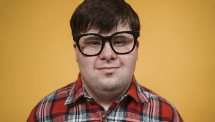 A man wearing glasses and a plaid shirt against a yellow backdrop.
